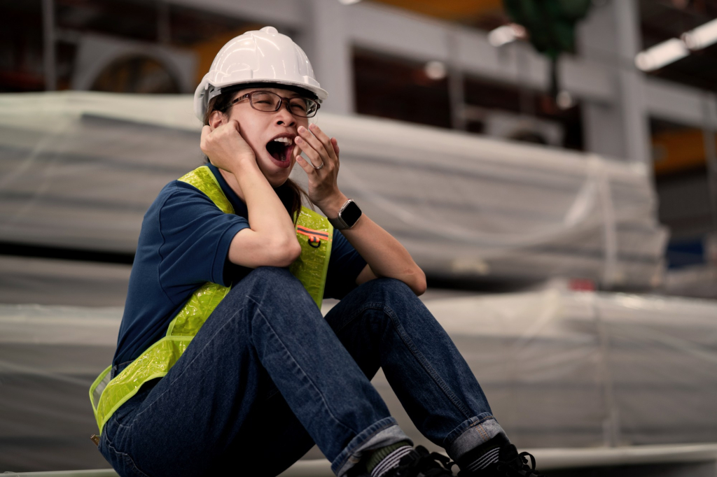 Trabajador industrial con casco y chaleco reflectante bostezando por fatiga y falta de sueño